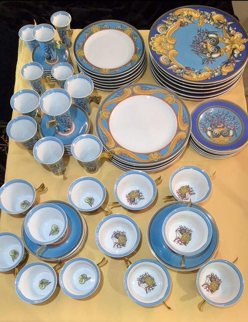 May include: A collection of fine china with a blue and gold design. The set includes plates, saucers, cups, and tall vases. The plates have a white center with a blue and gold border. The cups and vases have a blue background with gold accents.
