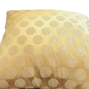 May include: A square, golden-yellow pillow with a repeating pattern of embossed, circular medallions. The medallions have a detailed, ornate design. The pillow has a soft, textured appearance, suggesting a comfortable, decorative item for home decor.