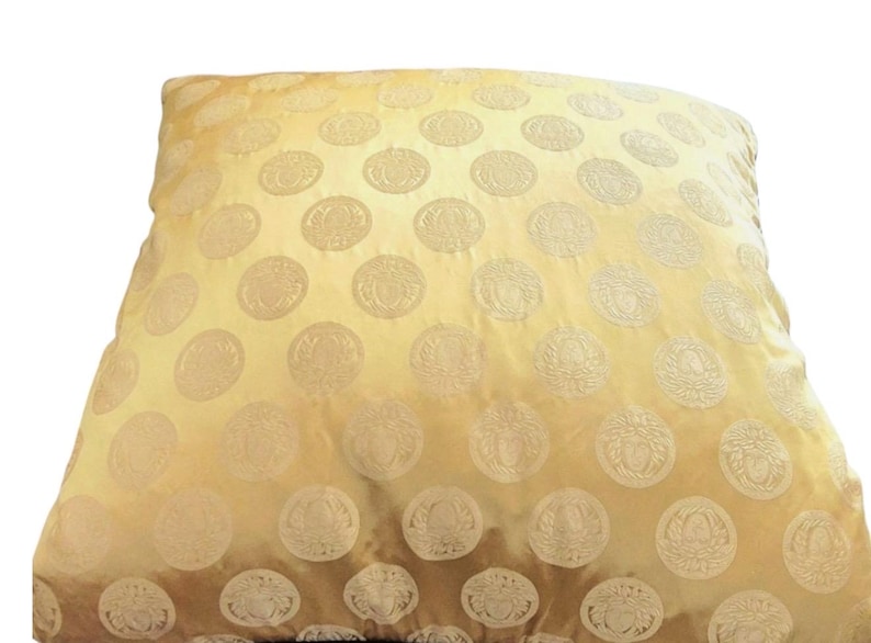 May include: A square, golden-yellow pillow with a repeating pattern of embossed, circular medallions. The medallions have a detailed, ornate design. The pillow has a soft, textured appearance, suggesting a comfortable, decorative item for home decor.