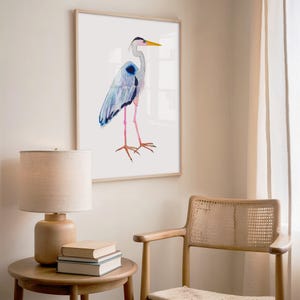 Puede incluir: Pintura a la acuarela de una garza enmarcada. El ave tiene plumas azules y grises, patas rosas y un pico amarillo. La obra de arte se exhibe sobre un fondo blanco, agregando un toque de decoraci&oacute;n inspirada en la naturaleza a la habitaci&oacute;n.