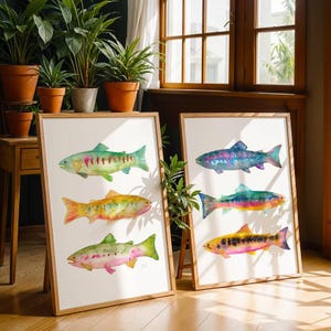 May include: Two framed watercolor prints featuring colorful fish illustrations. Each print displays three different fish, showcasing a variety of hues including green, yellow, pink, and blue. The frames are made of light-colored wood.