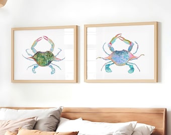 May include: Two framed watercolor crab art prints. One crab is green and blue, the other is blue and purple. The crabs have red claws and are set against a white background. The frames are light brown.