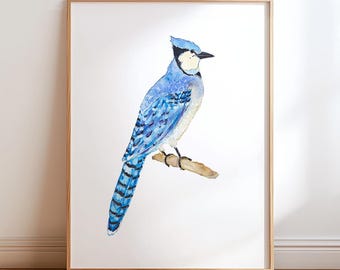 May include: Watercolor painting of a blue jay perched on a branch. The bird features shades of blue, black, and white, with detailed feather patterns. The artwork is framed in a light brown wooden frame, set against a white background.
