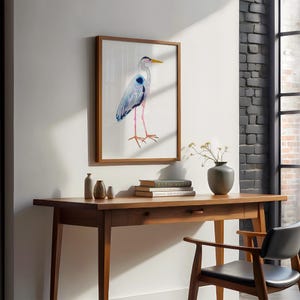 Puede incluir: Una impresi&oacute;n en acuarela enmarcada de una garza en tonos azules, grises y rosas. La obra de arte cuelga sobre un escritorio de madera con un caj&oacute;n, peque&ntilde;os jarrones, libros y un jarr&oacute;n gris con flores. Una silla de cuero negro est&aacute; colocada en el escritorio.