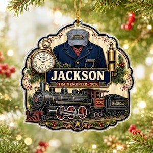 May include: A decorative ornament featuring a black steam locomotive, a pocket watch, and a train engineer uniform with a striped cap. The text reads JACKSON, TRAIN ENGINEER, and 2026. The design includes pine branches and a gold star.