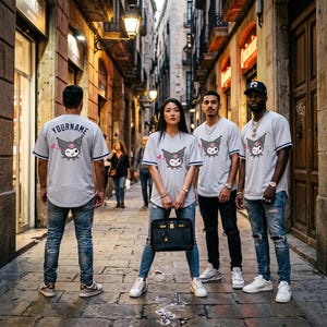 May include: Light gray short-sleeve jerseys featuring a graphic of a winking cartoon character with a pink heart. The back of one jersey displays the text YOURNAME. The garments are paired with blue denim jeans and white sneakers in a city street.