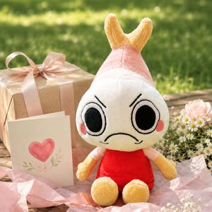 Puede incluir: Un peluche con cabeza blanca, detalles rosas y amarillos, y expresi&oacute;n enfadada. Viste una camiseta roja y tiene brazos y pies amarillos. Tambi&eacute;n hay una caja de regalo con lazo rosa y una tarjeta con dise&ntilde;o de coraz&oacute;n.