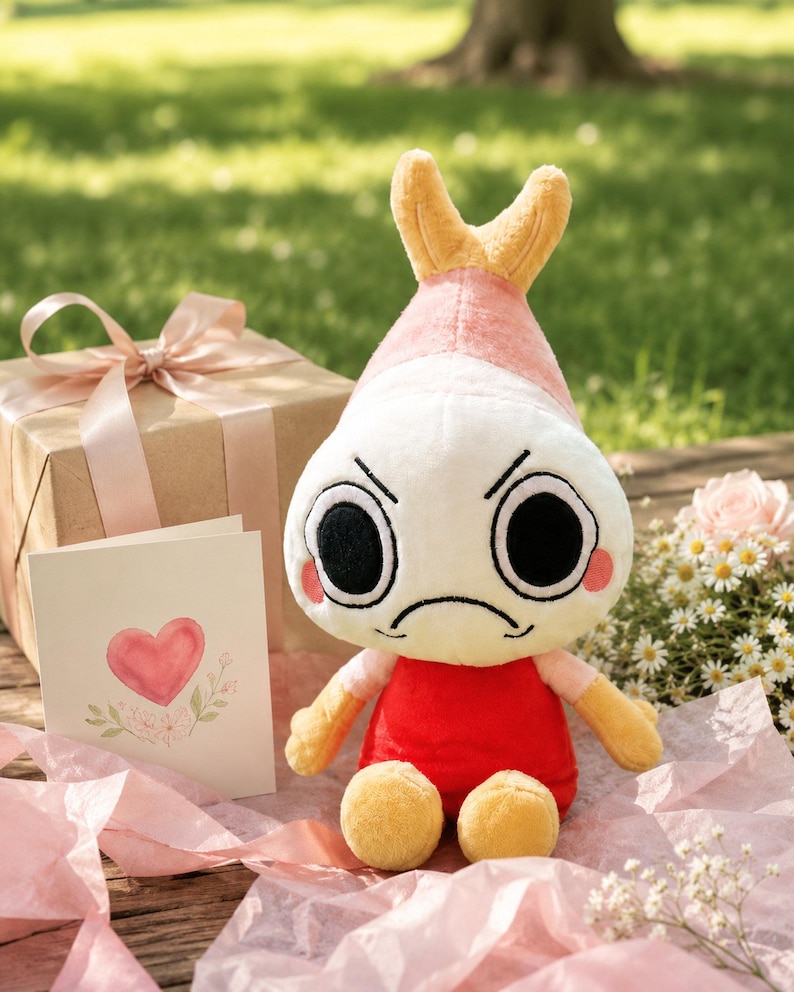 Puede incluir: Un peluche con cabeza blanca, detalles rosas y amarillos, y expresi&oacute;n enfadada. Viste una camiseta roja y tiene brazos y pies amarillos. Tambi&eacute;n hay una caja de regalo con lazo rosa y una tarjeta con dise&ntilde;o de coraz&oacute;n.