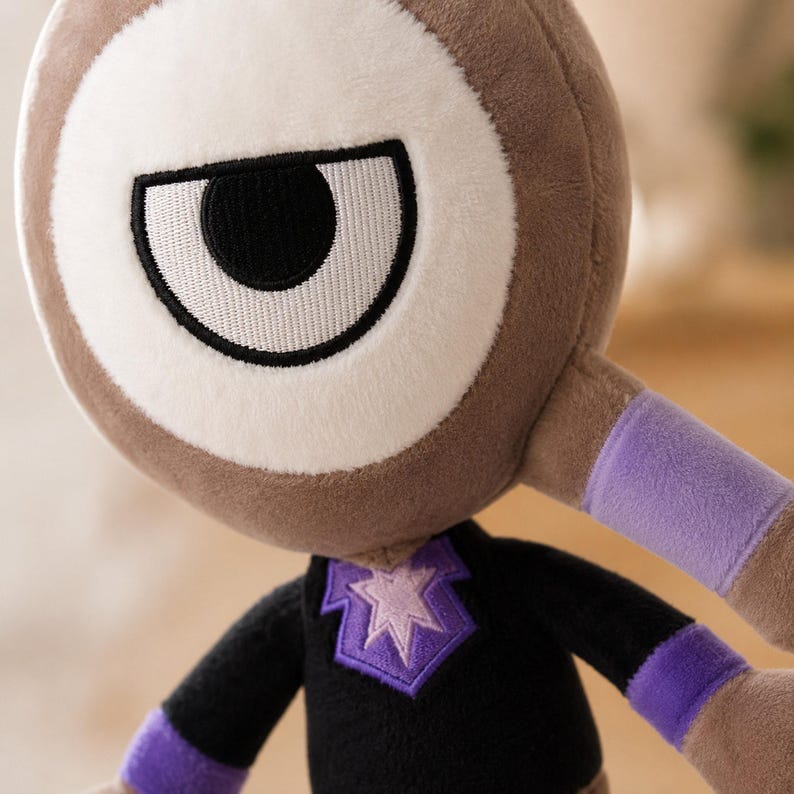May include: A plush toy with a large, stylized eye. The toy has a brown body, a white and brown eye, and a black shirt with a purple star design. Purple bands are on the arms. The toy is soft and cuddly.