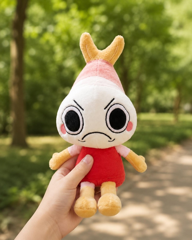 Puede incluir: Un peluche con forma de camar&oacute;n con una expresi&oacute;n de mal humor. El juguete tiene una cabeza blanca con ojos negros, mejillas rosadas y un vestido rojo. La cola y las extremidades del camar&oacute;n son amarillas.
