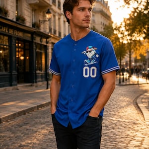 May include: A royal blue short-sleeved baseball jersey featuring a button-down front, white striped trim on the sleeves, and the number 00 printed in white. A graphic of a baseball character wearing sunglasses and a cap is positioned on the chest.