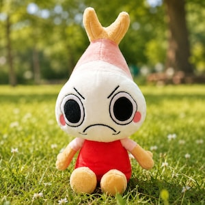 Puede incluir: Un peluche con forma de camar&oacute;n con una expresi&oacute;n de enfado. El juguete tiene una cabeza blanca, una parte superior rosa y amarilla, un cuerpo rojo y brazos y piernas peque&ntilde;os. Est&aacute; sobre hierba verde.