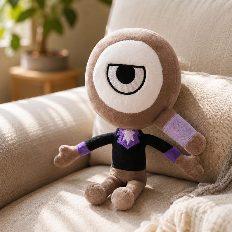May include: A plush toy with a large, round head featuring a white eye with a black pupil. The toy has a brown body, black shirt with a purple star design, and purple accents on the arms. It is sitting on a beige couch.