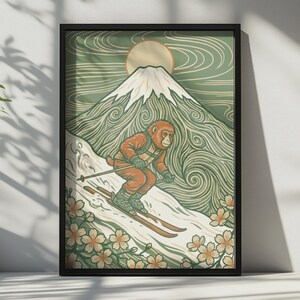 Könnte beinhalten: Gerahmter Kunstdruck mit einem Affen, der einen schneebedeckten Berg hinunterfährt. Die Illustration hat einen Vintage-Stil mit einer grünen und beigen Farbpalette. Der Affe trägt einen orangefarbenen Skianzug, und der Hintergrund zeigt eine Sonne und Kirschblüten.