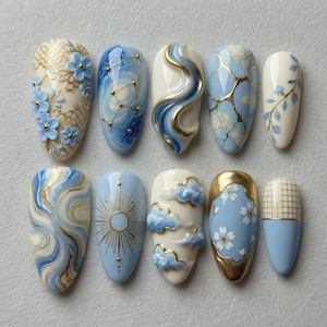 May include: A collection of ten artificial nails with various designs. The nails feature a range of colors, including light blue, white, and gold. Designs include floral patterns, celestial motifs, and abstract swirls. Some nails have 3D elements.