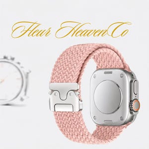 May include: A pink braided watch band attached to a silver-toned smartwatch case with a metallic buckle. The text Fleur Heaven Co is displayed in gold script above the watch. The watch features a circular sensor on the back and a side dial.