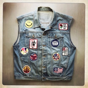 May include: A blue denim vest with various patches, including a peace sign, a smiley face, an American flag, and the text "Have a Nice Day".