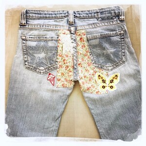 May include: Light blue denim jeans with floral and butterfly patches sewn on the back pockets.