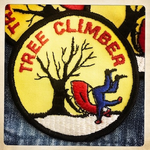 May include: A yellow embroidered patch with the text "TREE CLIMBER" in red. The patch features a black silhouette of a tree with a person sitting in a red chair.