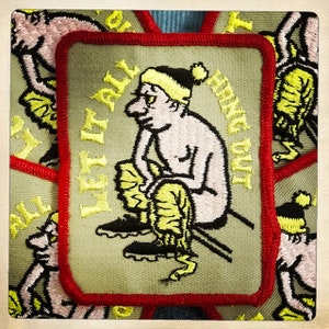 May include: A green embroidered patch with a red border. The patch features a cartoon illustration of a person wearing a yellow hat and sitting on a bench. The text "Left it all" is embroidered in yellow on the left side of the patch. The text "Hanging out" is embroidered in yellow on the right side of the patch.
