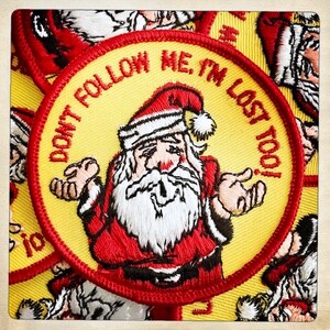 Puede incluir: Un parche bordado amarillo y rojo con un Papá Noel de dibujos animados. El texto en el parche dice "No me sigas, ¡estoy perdido también!"