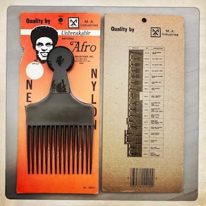 May include: A black plastic comb with a wide handle and a row of teeth. The comb is packaged on a red and orange card with the words "Unbreakable Afro" and "Nylon" printed on it. The card also features a black and white image of a man with an afro.