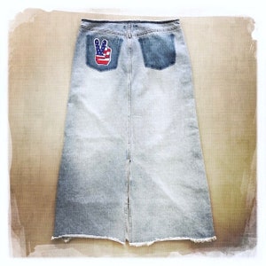 May include: A light blue denim skirt with a back pocket featuring a peace sign patch with an American flag design.