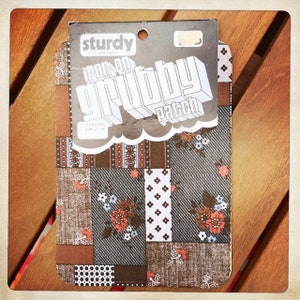 May include: A package of iron-on patches with a brown, gray, and white patchwork design. The package says "Sturdy Brand Iron-On Gribby Patch" and "2 Patches 3 in. x 3 in."