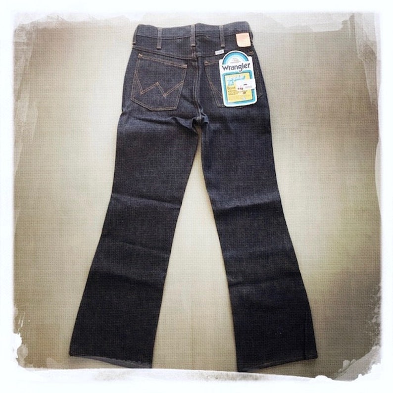 May include: A pair of dark blue denim jeans with a wide leg opening. The jeans have a label on the back pocket that says "Wrangler" and "Boot Cut".
