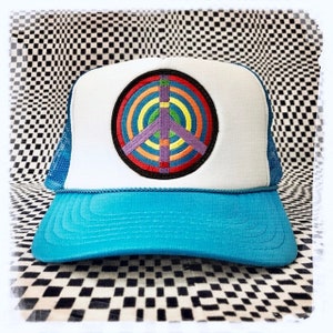 Puede incluir: Una gorra de camionero azul y blanca con un signo de paz arcoíris bordado en la parte delantera.