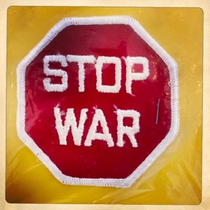 May include: A red stop sign with white stitching around the edges. The sign says "STOP WAR" in white letters.