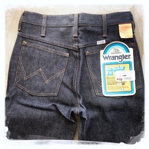 May include: A pair of dark blue denim jeans with a back pocket featuring a stitched 'W' logo. The jeans have a label on the back pocket that reads 'Wrangler Regular Fit Boot Wrangler 100% Cotton 14 Ounce Denim with'.