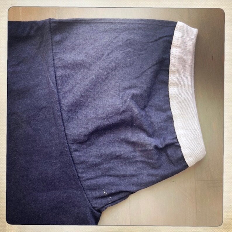 Op de afbeelding: Een donkerblauw t-shirt met een witte geribbelde rand rond de hals en mouwen.