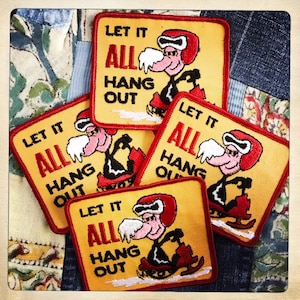 May include: Four yellow and red embroidered patches featuring a cartoon character riding a snowmobile. The patches say "Let it all hang out".
