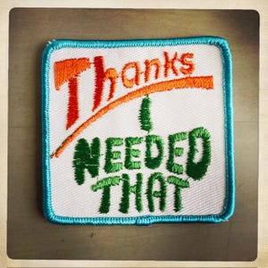 May include: A white embroidered patch with a blue border. The patch says "Thanks I Needed That" in green and orange lettering.