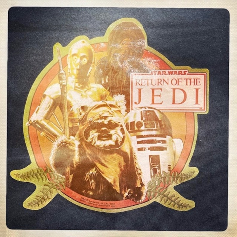 Op de afbeelding: Een vintage Star Wars: Return of the Jedi strijkbadge met Chewbacca, C-3PO, R2-D2 en een Wookiee. De badge is geel, oranje en rood met een zwarte achtergrond.