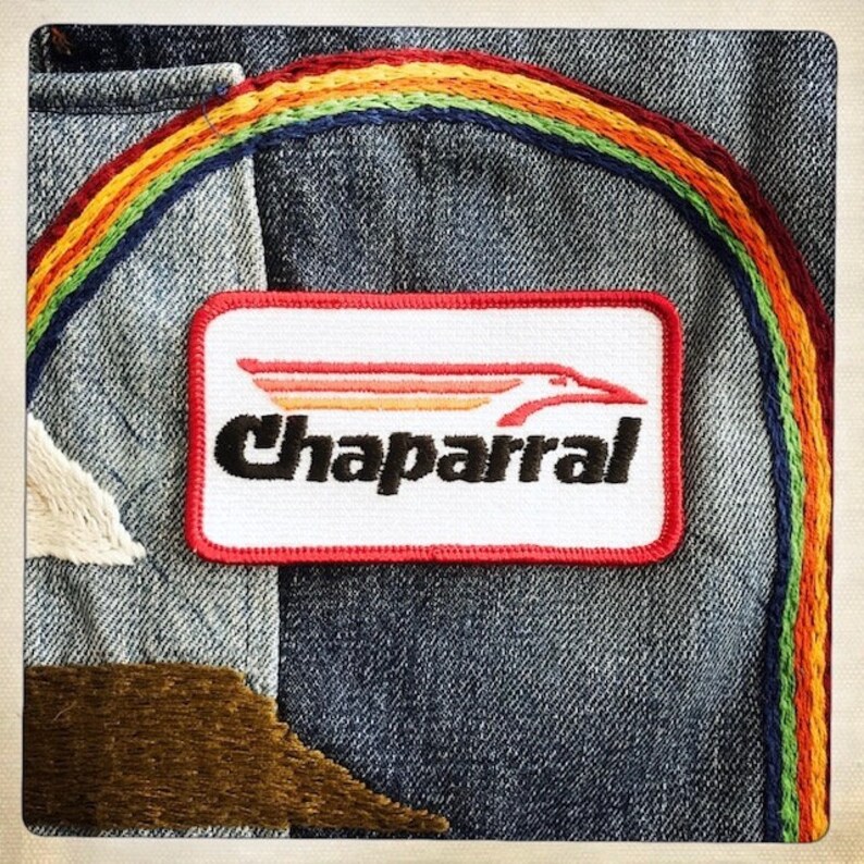 Puede incluir: Una chaqueta vaquera con un parche bordado de arco&iacute;ris y un parche bordado de rojo, blanco y negro que dice "Chaparral".