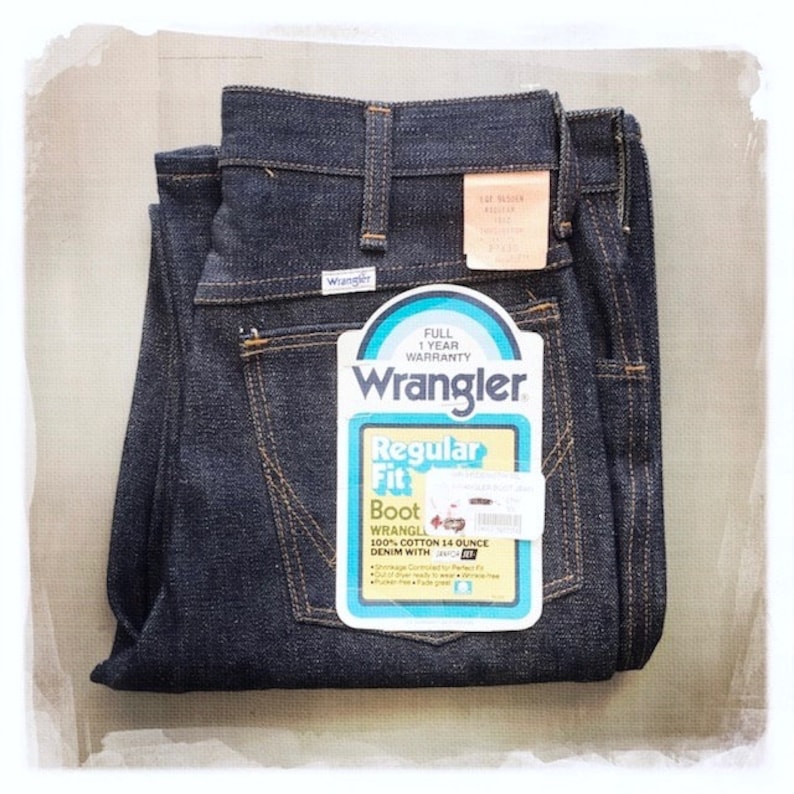 May include: A pair of dark blue denim jeans folded in half. The jeans have a label that says "Wrangler Regular Fit Boot Wrangler 100% Cotton 14 Ounce Denim with" and a smaller label that says "Full 1 Year Warranty Wrangler".