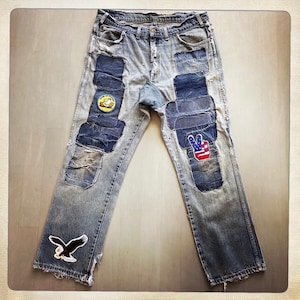 Può includere: Un paio di jeans blu denim con diversi patch cuciti. I patch sono realizzati in diversi tessuti e colori, tra cui denim, velluto a coste e tela. I jeans hanno un aspetto consumato, con strappi e lacrime nel tessuto. I patch includono un segno di pace con un design di bandiera americana, un'aquila calva e un personaggio dei cartoni animati giallo.