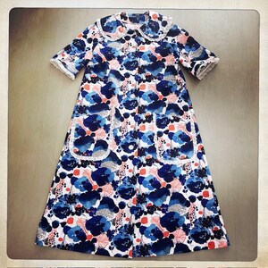 May include: A white, blue, and pink floral print robe with a white lace trim around the collar, sleeves, and pockets. The robe has a button-up front and short sleeves.