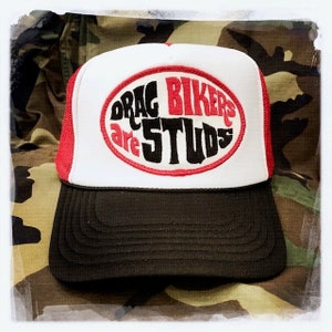 May include: A red and white trucker hat with a black oval patch that says "Drag Bikers Are Studs".