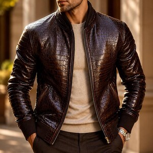 May include: A dark brown bomber jacket with a glossy crocodile skin texture, featuring a ribbed collar, cuffs, and hem. The jacket is worn open over a light beige crew neck sweater, revealing a central metal zip and two side pockets.