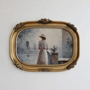 Puede incluir: Pintura enmarcada de forma ovalada con un borde dorado ornamentado. La obra de arte representa a una persona con vestido y sombrero, de pie en una terraza, con un jarrón de flores. La pintura tiene una paleta de colores suaves y apagados.