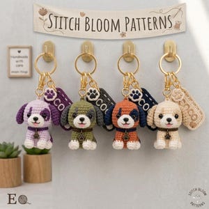 Può includere: Quattro portachiavi a forma di cucciolo all'uncinetto nei colori viola, verde, arancione e crema, ciascuno con un portachiavi color oro. I portachiavi sono appesi a ganci dorati. Lo striscione sopra recita "Stitch Bloom Patterns".
