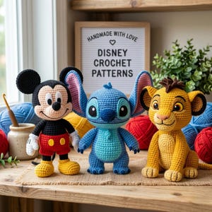 Può includere: Tre bambole di personaggi Disney all'uncinetto: Topolino, Stitch e Simba. Topolino è nero, rosso e giallo. Stitch è blu. Simba è giallo e marrone. Le bambole sono esposte su una superficie di legno con filato e un cartello con la scritta "Handmade with Love Disney Crochet Patterns."