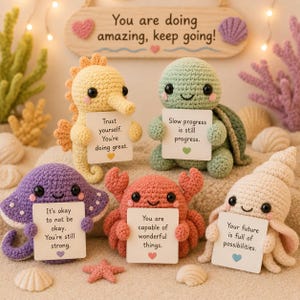 May include: A collection of crocheted sea creatures, including a seahorse, turtle, stingray, crab, and seashell, each holding a sign with an inspirational message. The sign above reads "You are doing amazing, keep going!"
