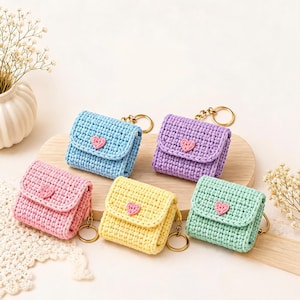 May include: Five small, square, crocheted cases with flap closures and gold-tone key rings. Each case features a single pink heart embellishment on the front flap. The cases are colored light blue, lavender, pink, yellow, and mint green.