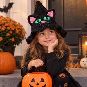 Può includere: Un cappello da strega lavorato all'uncinetto nero con orecchie da gatto con dettagli interni rosa, occhi da gatto verde brillante e un piccolo naso rosa con baffi bianchi. Il cappello ha una punta conica e una tesa larga e ondulata.