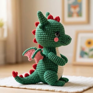 Può includere: Un drago all'uncinetto verde fatto a mano con dettagli rossi sulla schiena e sulla coda. Il drago ha ali rosa e una pancia color crema. Ha occhi neri e guance rosa. Il drago è seduto su una superficie bianca.