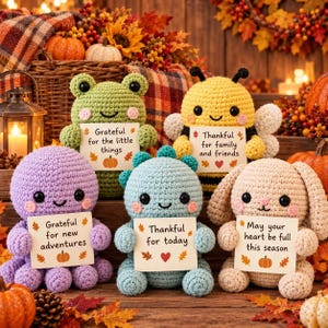 Puede incluir: Cinco peluches de ganchillo que incluyen una rana verde, una abeja amarilla, un pulpo morado, un dinosaurio azul y un conejo beige. Cada juguete sostiene un cartel blanco con texto: Grateful for the little things, Thankful for family and friends, Grateful for new adventures, Thankful for today y May your heart be full this season.